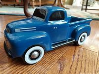 Side view showing detailed blue ceramic Ford F-1 truck with whitewall tires and silver hubcaps on a wooden floor.