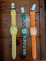 Top down photo of three women's watches laid out, yellow, turquoise with monkey design, and orange silicone bands, lock pins on.