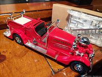 Close-up image of the red diecast 1937 Ahrens-Fox fire truck coin bank showing chrome details and black seats on wooden surface.