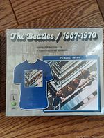 Front of sealed package showing The Beatles 1967-1970 remastered CD set and the blue T-shirt featuring album artwork.