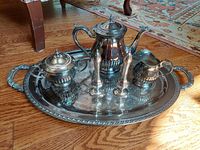 Photo showing entire tea set arranged on silver plate tray on wooden floor with carpet background.