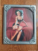 Front view of vintage pin up girl print in pewter frame on wooden floor.