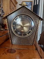 Front view shows pentagonal brass and wood clock face with wavy decoration and clear dome glass with brass frame. The dial reads 'Atlanta' with Arabic numerals.