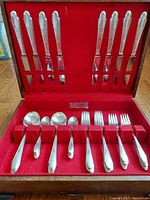 Full view of multiple silver plated knives, spoons, forks stored in red velvet compartmentalized box