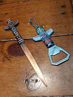 Two vintage First Nations imagery items: a letter opener with totem pole handle and a bottle opener with totem pole design and chain, both placed on wooden surface.