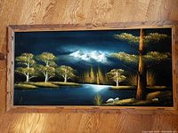 Full front view of black velvet landscape painting showing the overall composition with golden trees, river, mountains, and wood frame.