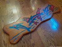 Top view of the wooden carving showing detailed dolphin designs and traditional Nuxalk First Nations style colors and patterns on wood.