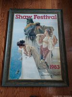 Front view of framed Shaw Festival poster displayed on a wood floor showing full poster with title and date information.