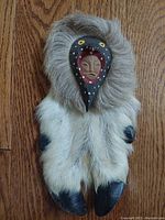 Wood carved face mask mounted on a fur-covered ungulate hoof, showing front details.