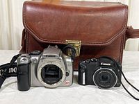 Front view of Canon EOS Rebel DS6041 DSLR camera body (no lens), Canon SX170 IS compact camera, and brown Minolta vinyl camera bag.