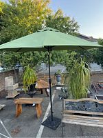 Full view of the green patio umbrella opened with metal base stand, surrounded by outdoor plants and furniture.