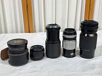 Five camera lenses placed standing on a white surface showing variety of sizes and designs.