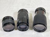 Three Soligor camera lenses of varying focal lengths laid out side by side, showing their barrels and glass elements.