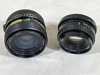Photo showing two Vivitar camera lenses side by side on a flat surface, clearly showing size and markings