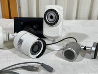 Three security cameras (two bullet style and one dome style) and one older model Ring video doorbell shown together on a white surface.