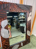 Front view of the decorated composite mirror reflecting warehouse shelves and chair.