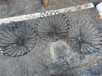 Set of three black metal wire hanging planters arranged side by side on asphalt surface showing their overall size and design.