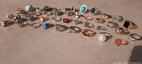 Photo showing full collection of 40 assorted rings laid out on a flat beige surface with varied styles and gemstone colors.