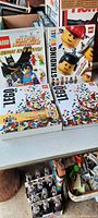 Four LEGO books displaying titles and colorful LEGO brick and mini-figure covers, two stacked upright and two laid flat.