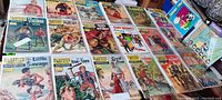 Top down view of 27 vintage comic books spread out on a table showing covers with western, action, and literary classic themes