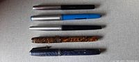 Five vintage ink pens laid out on a light background showing variety in design and color.