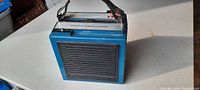 Front view of vintage blue portable 8 track tape player with leather carry handle and speaker grill.