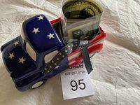 Blue ceramic truck with white stars on the cab and bed, holding rolled and bundled 1976 currency and coins, set on a white fabric background.