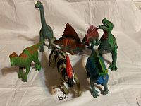 Seven assorted dinosaur toys arranged in a group including various colors and species.