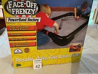 Photo of Face-Off Frenzy PowerBand Hockey game box showing the game set and features like portability and play on multiple floor surfaces.