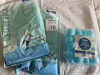 Two KOMAX Ice Tank Packs and one package of two KOMAX Bubble Ice Packs shown together on a cloth surface.