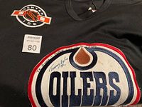 Close-up of the signed Edmonton Oilers logo on the black hockey jersey featuring inscription and autograph by player Timmy with 50 years message, showing some stains on the logo area.