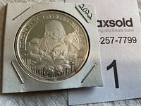 Front view of the 2022 Merry Christmas silver round depicting Santa Claus with pine branches and holiday bells, held inside a cardboard protective case.