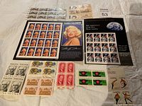 Photo of various full sheets and blocks of collectible stamps including Marilyn Monroe, Moon landing anniversary, historical portraits, and US wildlife stamps spread on a surface.