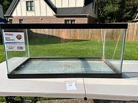 Front view of the 40 gallon glass aquarium on a table outside with grassy background.