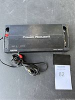 Top view of the black Power Acoustik amplifier with model number and brand visible, showing light wear and included RCA cable.