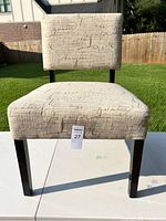 Front view of fabric upholstered chair with script text pattern and dark wooden legs