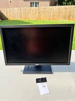 Front view of the black Dell computer monitor with rectangular screen and attached base stand outdoors on a table.