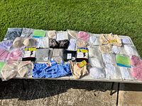 Wide view of a large assortment of folded and packaged brand new maternity bras, underwear, nursing pads, and other clothing items laid out on a table outdoors.
