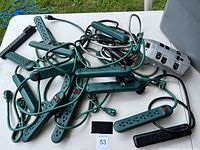 Top-down view of a pile of green surge protector power strips with cords and plugs in tangled arrangement.