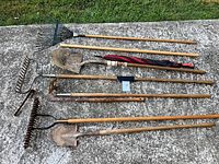 Full view of all yard tools laid out on pavement including rakes, shovels, garden fork, and umbrella
