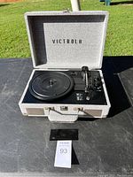 Full view of portable record player open, showing turntable, tonearm, control knobs, and interior lid branding.