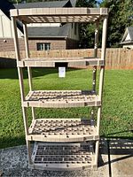 Front view of beige plastic tall shelving unit outdoors on grass with five grid-pattern shelves.