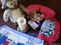 Weighted penguin, partially used candle on decorative base, artificial poinsettias, and red heart-shaped placemats on wooden surface with Christmas themed items.
