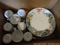 Top view of Corelle mugs and bread plates showing underside Corelle logos and some with fruit pattern edges.
