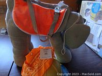 Elephant costume viewed from the side showing orange saddle cloth and bandana next to it on floor, highlighting soft fabric and foam padding.