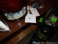 Show the Bissell vacuum cleaner on the right, Black & Decker iron on the left, and wooden musical bell box in the background on a wooden surface.