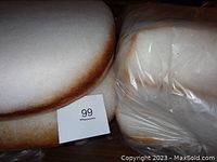 Four new foam chair cushions stacked together, showing rounded front and straight back edges with brown adhesive marks and plastic wrapping.