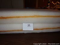 Two stacked foam cushions with a small label indicating lot number 98, showing white foam with orange-brown internal discoloration bands.
