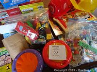 Photo of assorted toys including bongo drums, helmets, and bags with small plastic toys and vehicles.