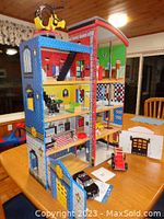 Full view of the multi-level police and fire station playset showing side with colorful walls, windows, doors, and the red fire truck and black police car seen parked in slots.